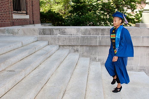 A student in a cap and gown walks up the stairs to Foellinger Auditorium